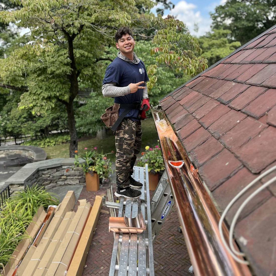 Shelby Roofing Services crew member beside a newly installed copper half-round gutter on a slate roof
