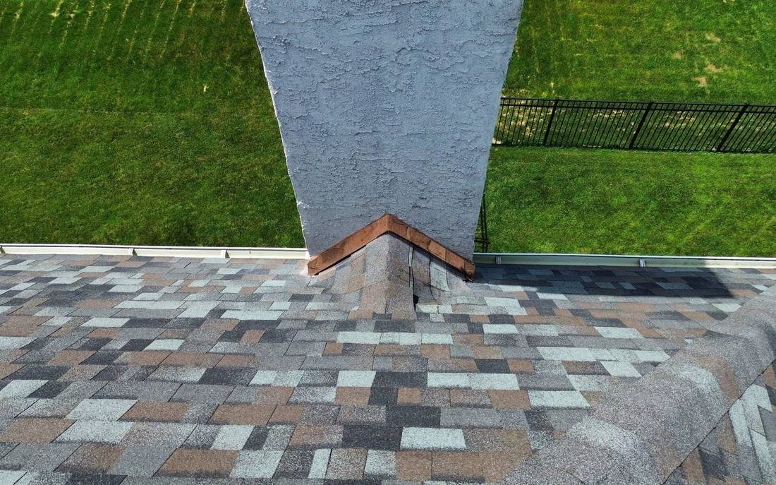 A shingled chimney cricket with copper flashing following its peak behind a stucco chimney, Shelby Roofing Services project in Plymouth Township, PA