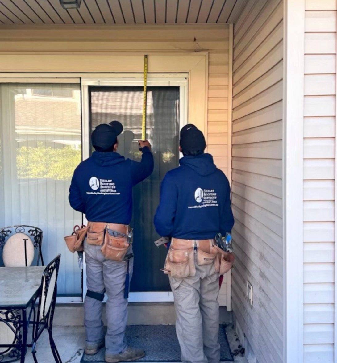 Shelby Roofing Services crew measuring a door opening on a vinyl-sided home