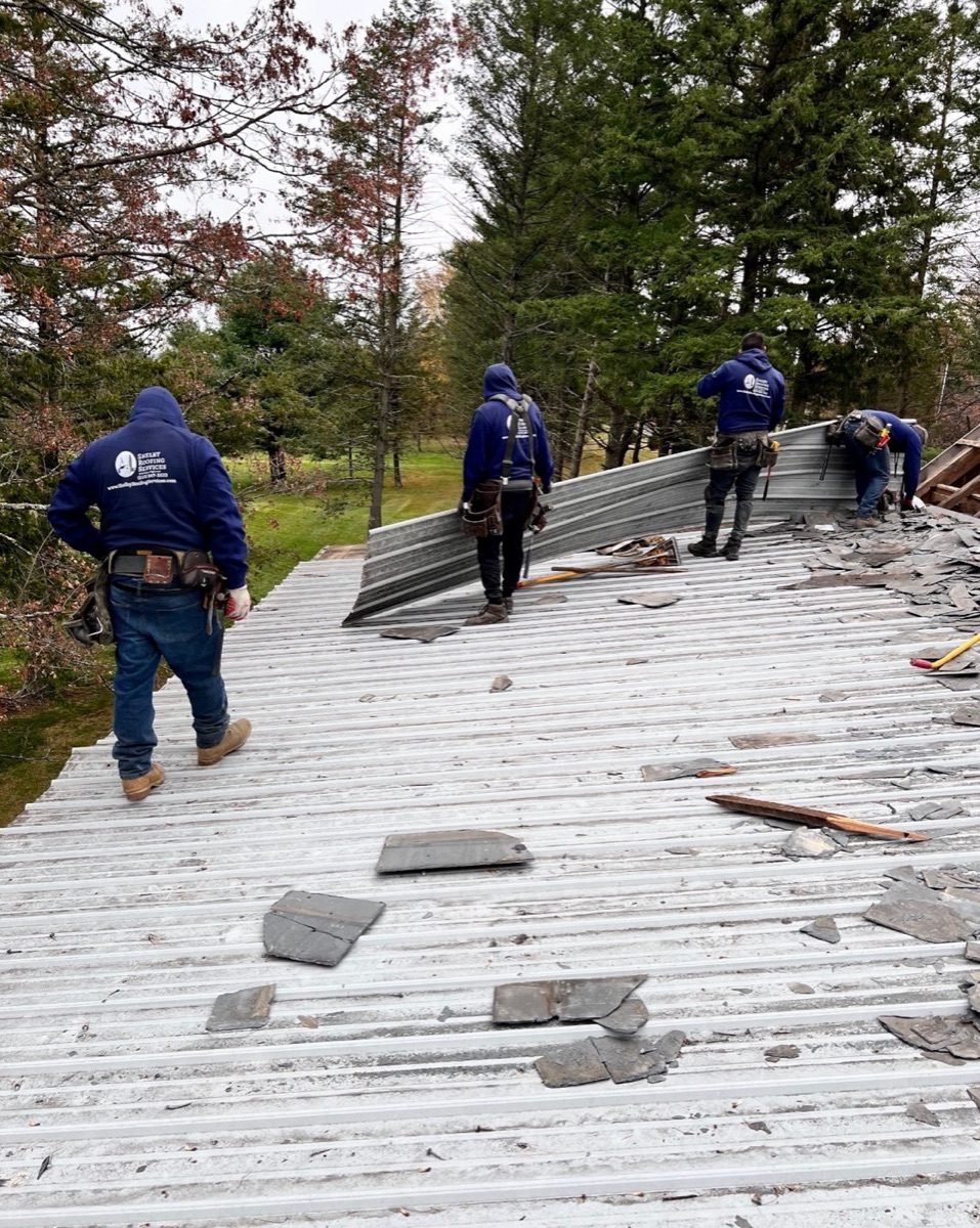 Four Shelby Roofing Services crew members working on a standing seam metal roof replacement