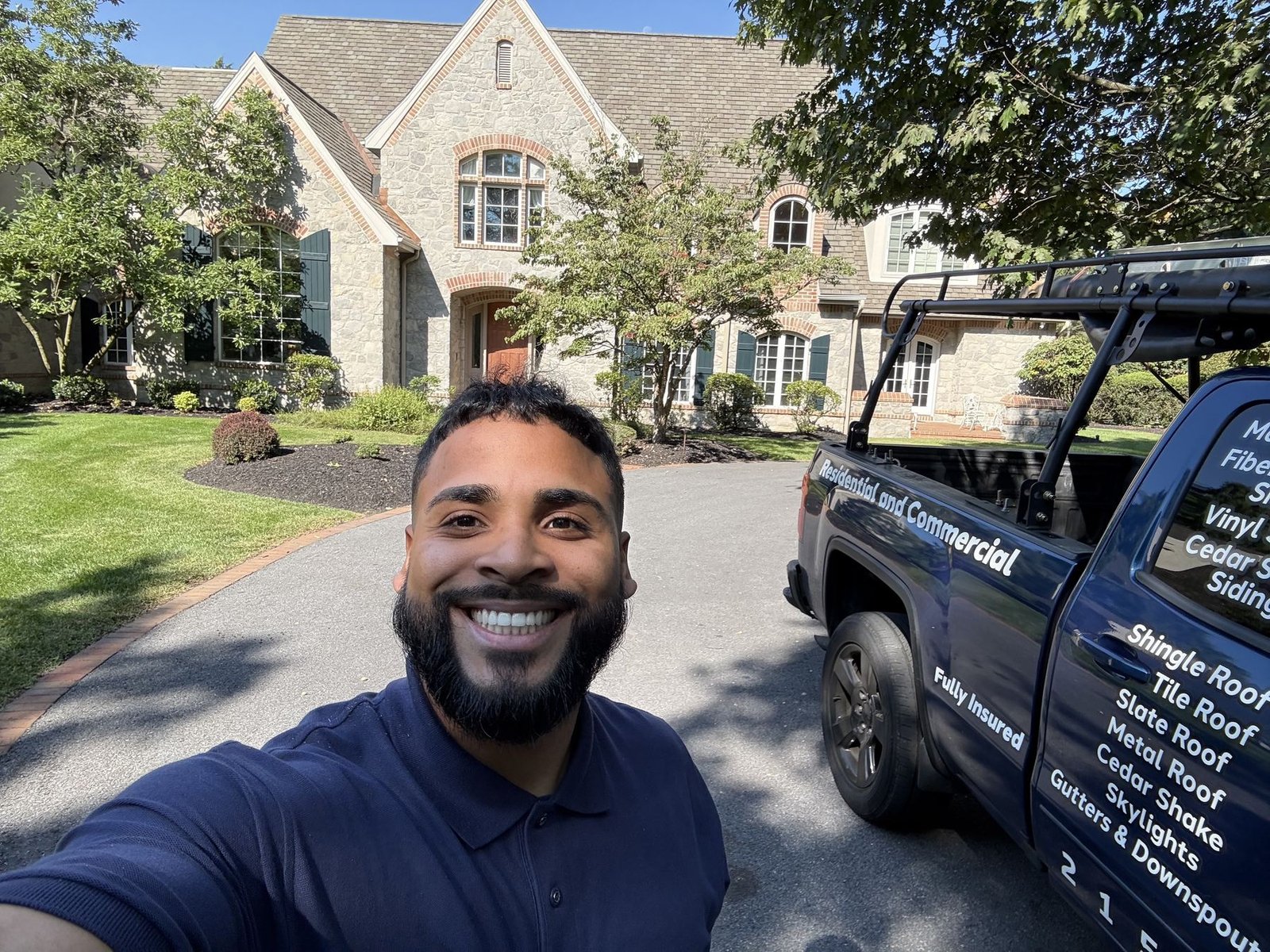 Miguel Cespedes with Shelby Roofing Services truck in front of a luxury stone colonial home
