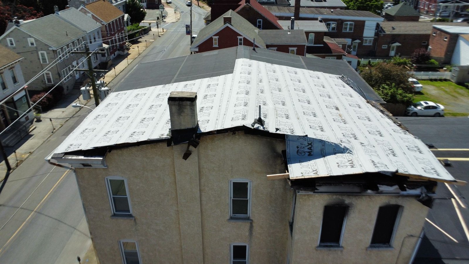 Before — close-up of fire-damaged adjacent building with emergency roof wrap and burn marks, PA