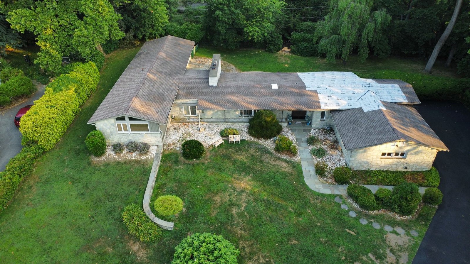 Before — front aerial of mid-century stone ranch with blue tarps over damaged roof, PA