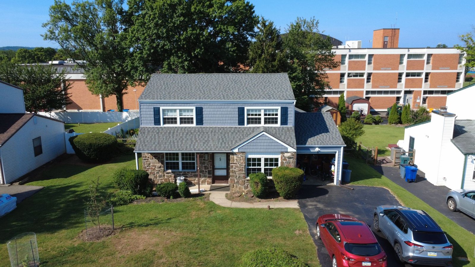 After — front aerial of stone colonial with new blue siding and gray shingles — Shelby Roofing Services PA
