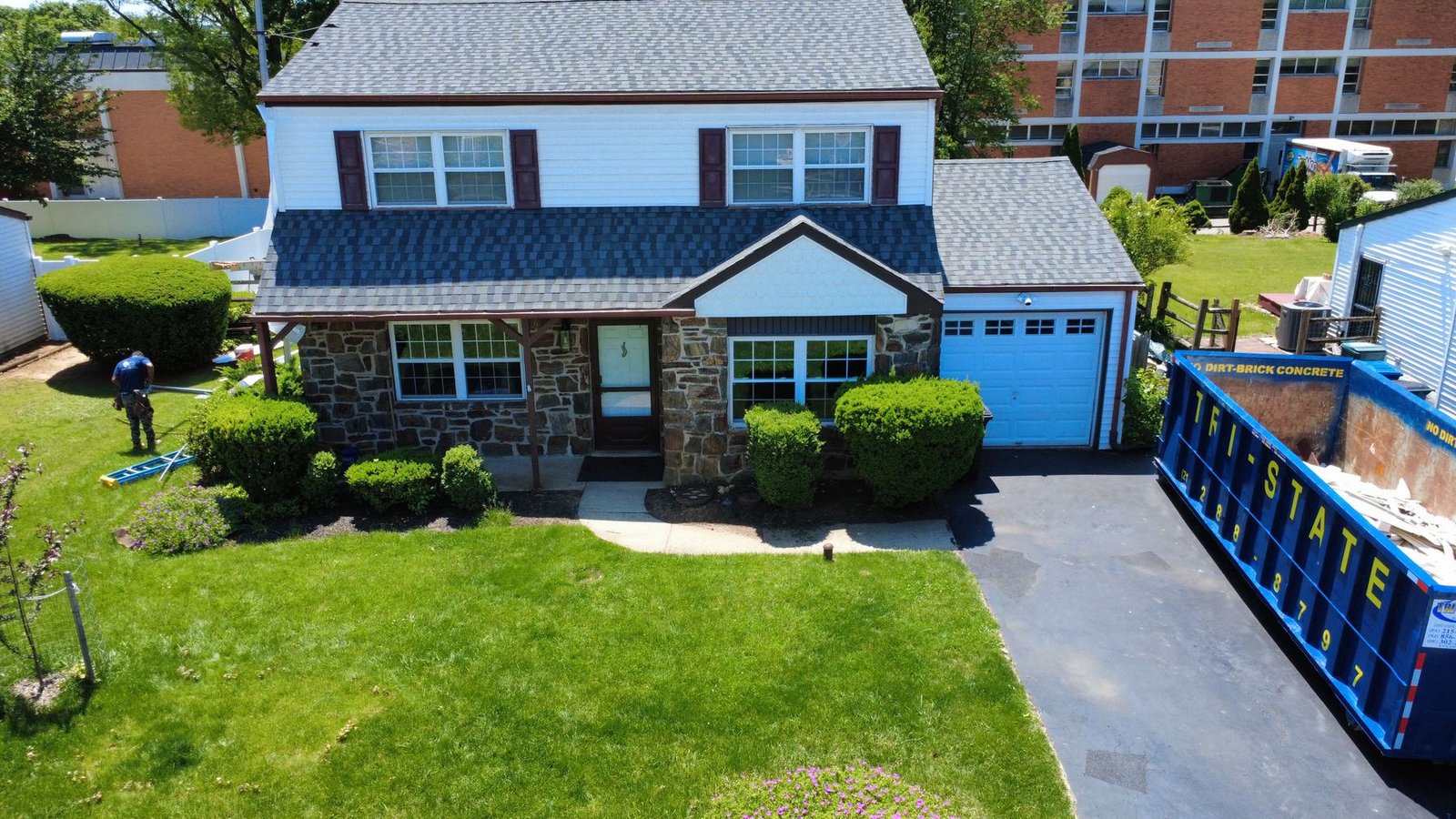 Before — front aerial of stone colonial with old dark shingles and Shelby dumpster, PA