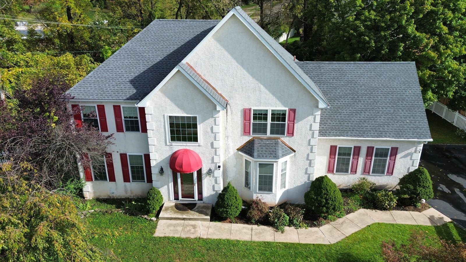 After — front of stucco colonial with new gray shingle roof, red shutters and copper flashing on the gable and bay window, Plymouth Meeting PA — Shelby Roofing Services