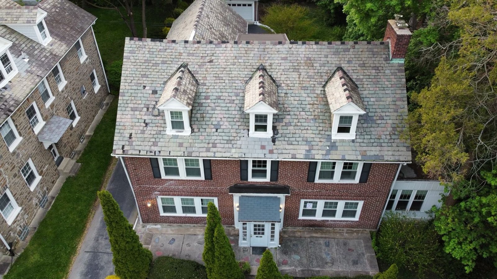 Before — front aerial of brick colonial with worn shingle roof and dormers, PA