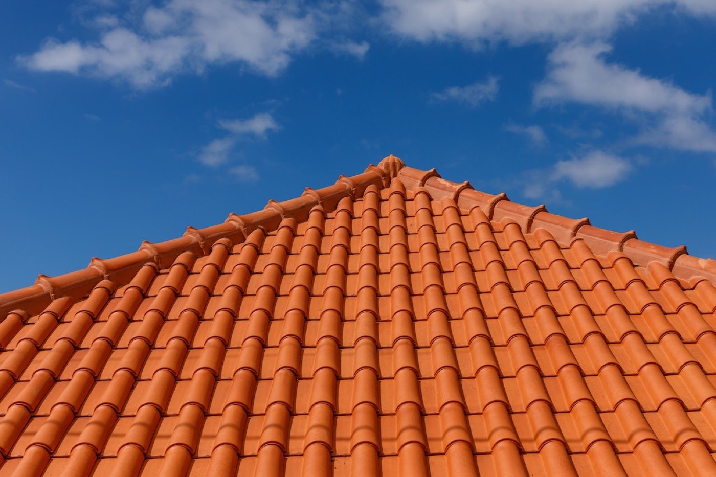 Traditional Spanish clay barrel tile roofing — terracotta curved tile courses and ridge detail against blue sky